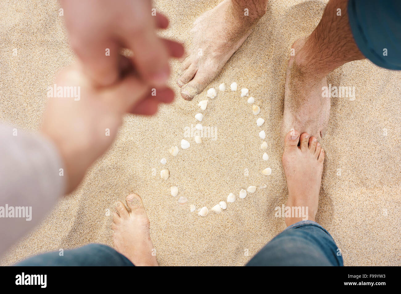 Weibliche und männliche Füße Nahaufnahme von Frau und Mann Hand in Hand und stehen neben der Schale Herz am Sandstrand Stockfoto
