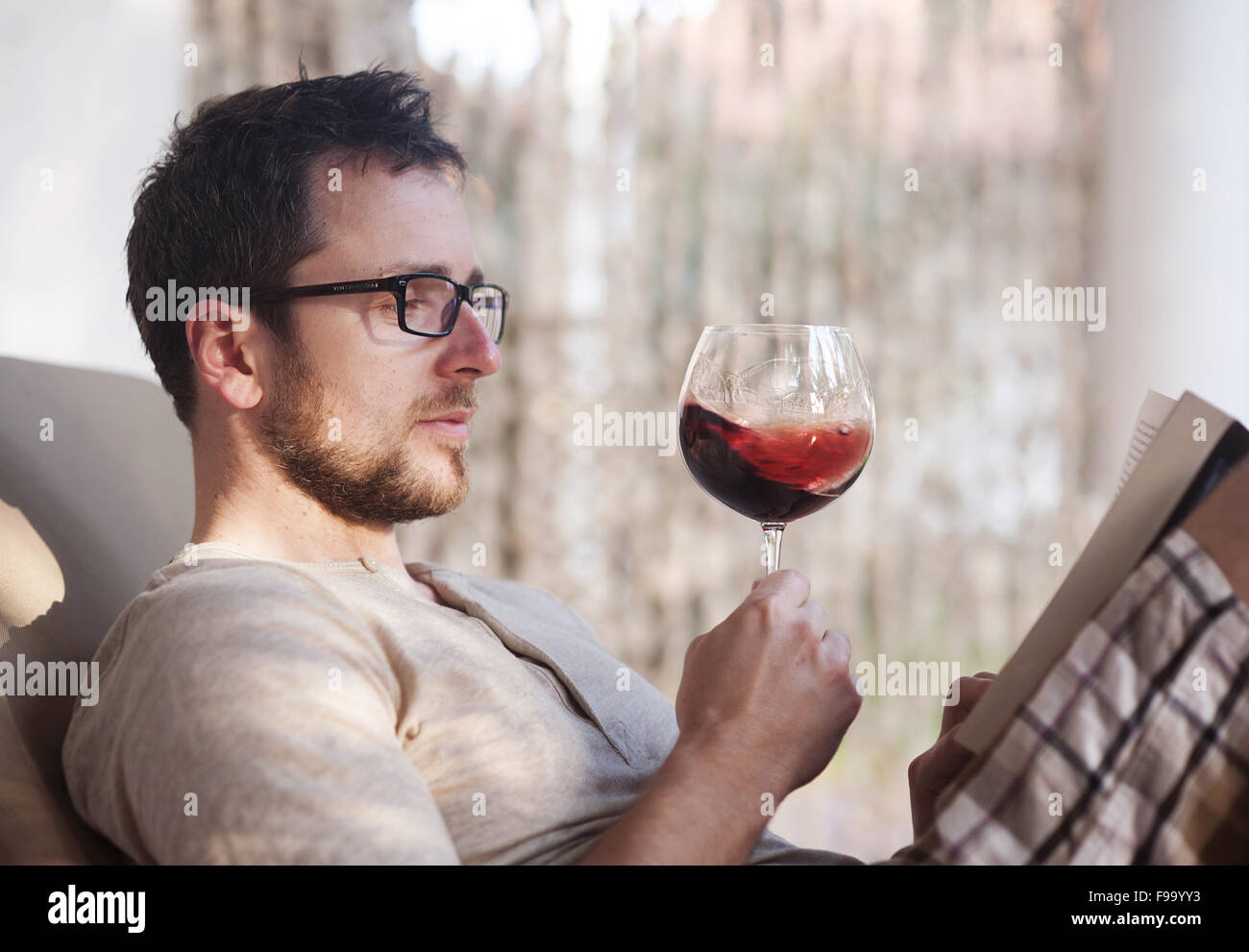 Hübscher Jüngling, entspannen, lesen und trinken Rotwein Stockfoto