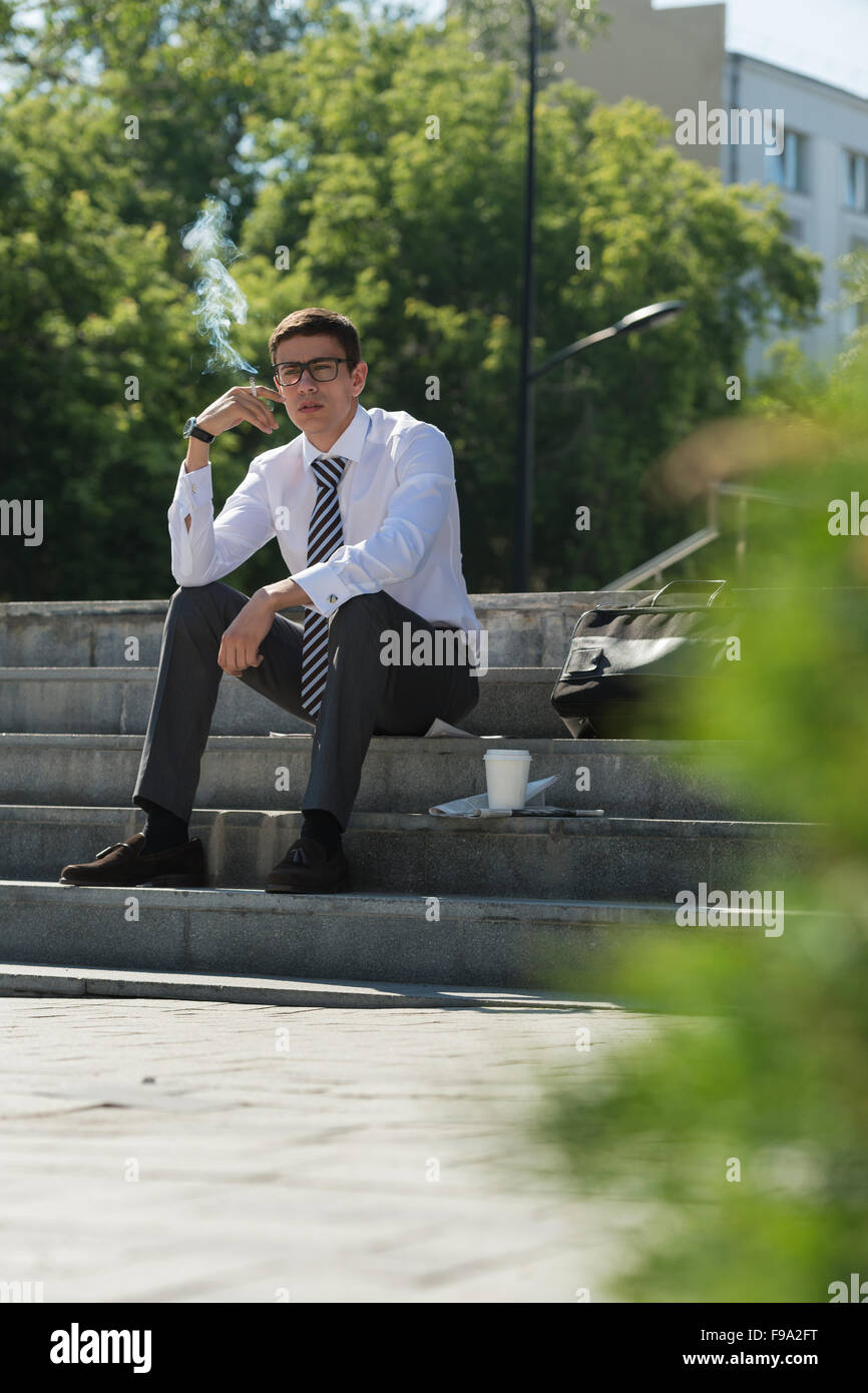 Gut gekleidete Business-Mann Rauchen sitzen auf einer Straße Bürgersteig Stockfoto