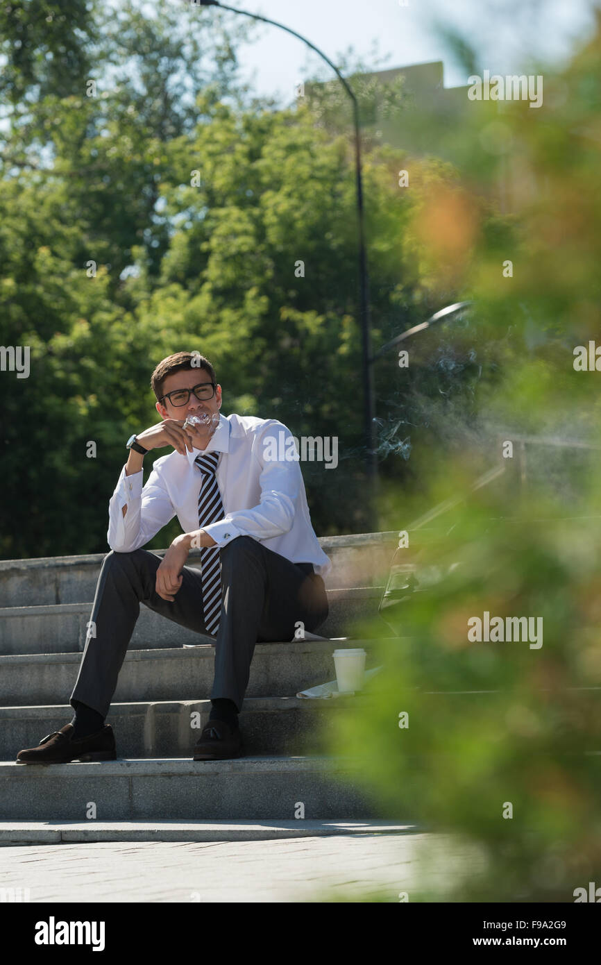 Gut gekleidete Business-Mann Rauchen sitzen auf einer Straße Bürgersteig Stockfoto