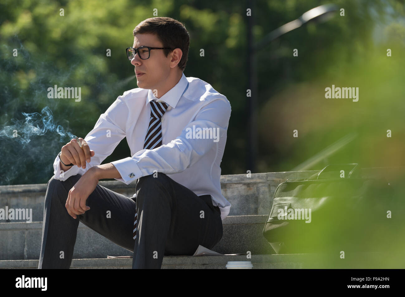 Gut gekleidete Business-Mann Rauchen sitzen auf einer Straße Bürgersteig Stockfoto