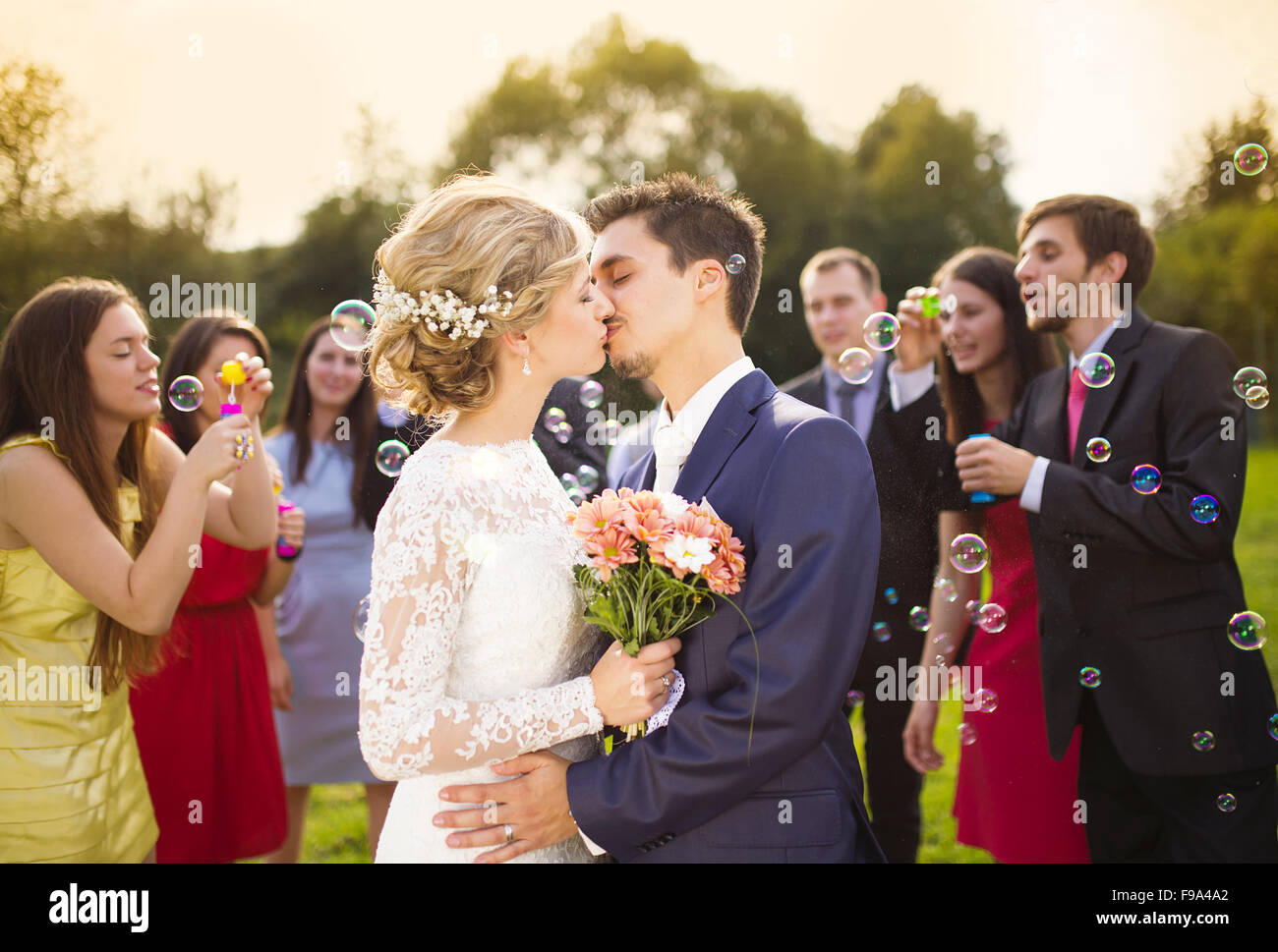 Junge Brautpaar küssen und genießen Sie romantische Momente zusammen auf Hochzeit außerhalb Gäste Hochzeit im Hintergrund weht Stockfoto