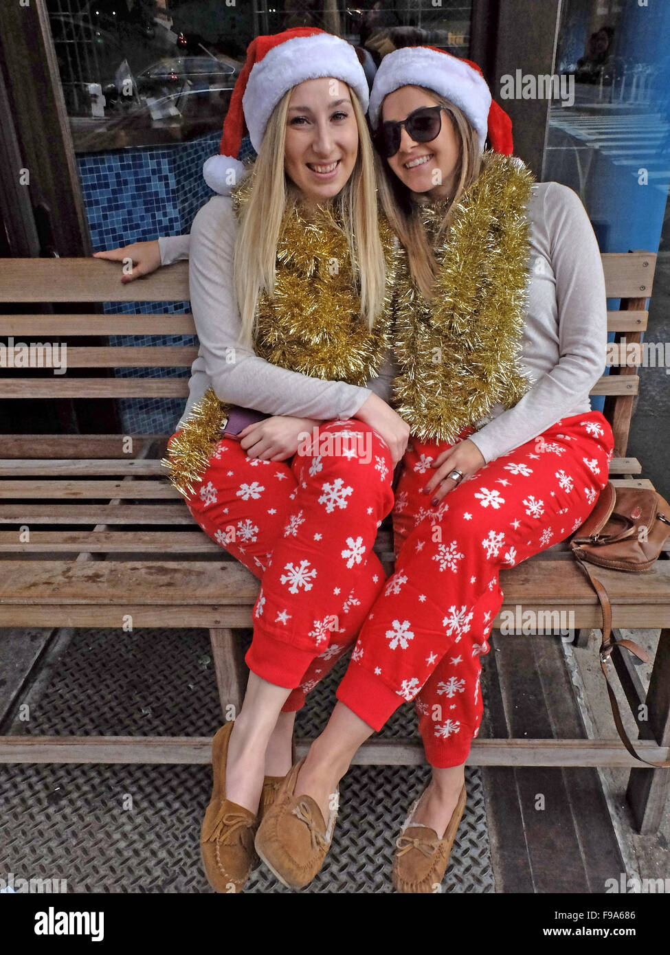 2 hübsche junge Damen in identischen Weihnachtsoutfits sitzen auf einer Bank in Chelsea, bevor Sie zu Santacon. Stockfoto