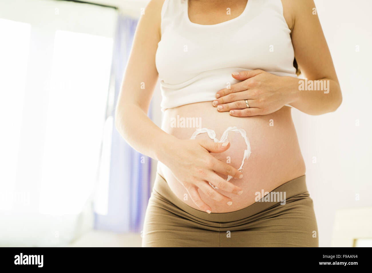 Porträt von schöne schwangere Frau mit Herzform aus Sahne auf den Bauch Stockfoto