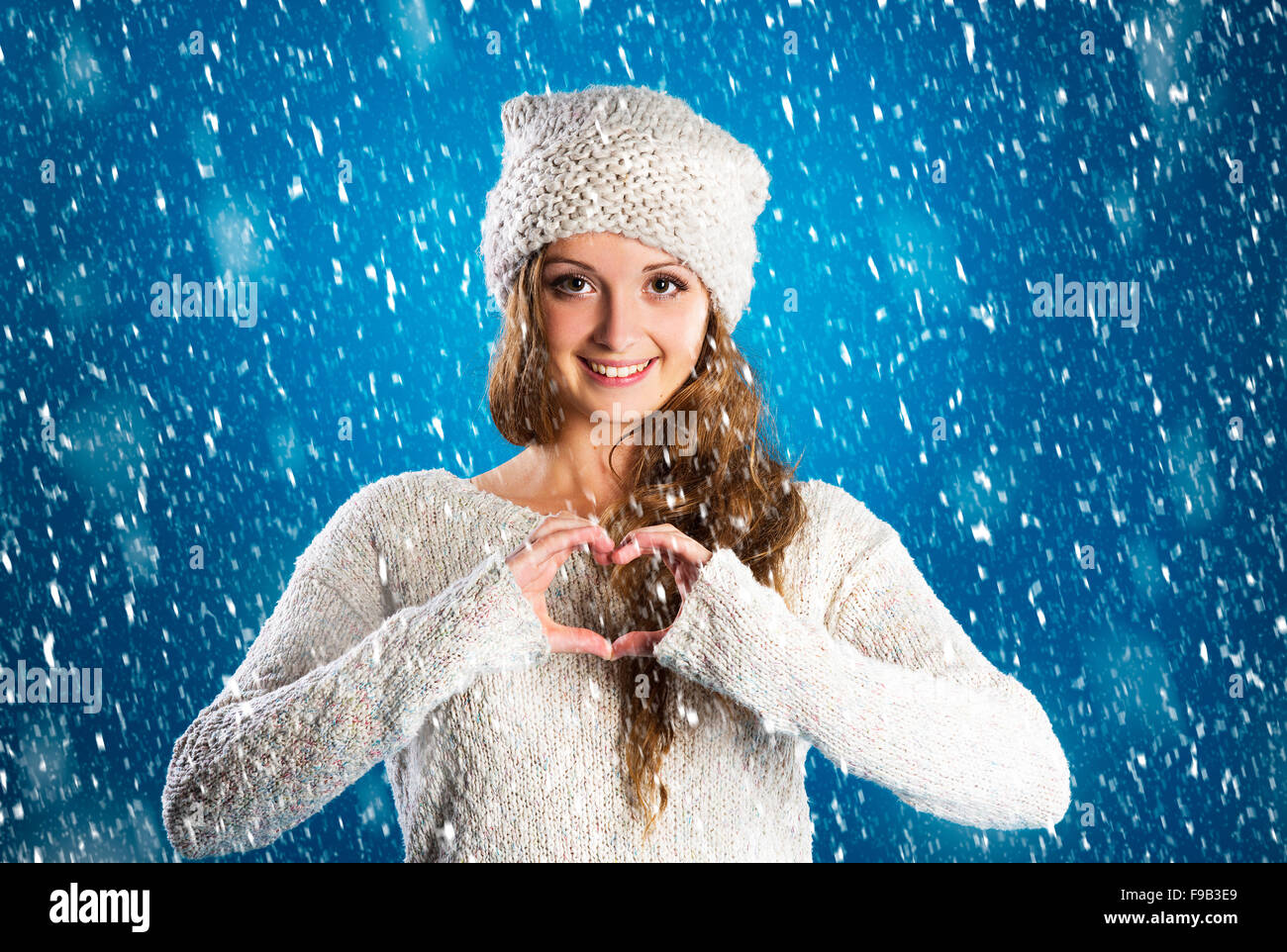 Schöne Frau im warmen Pullover mit Schneeflocken um sie herum, auf blauem Hintergrund Stockfoto