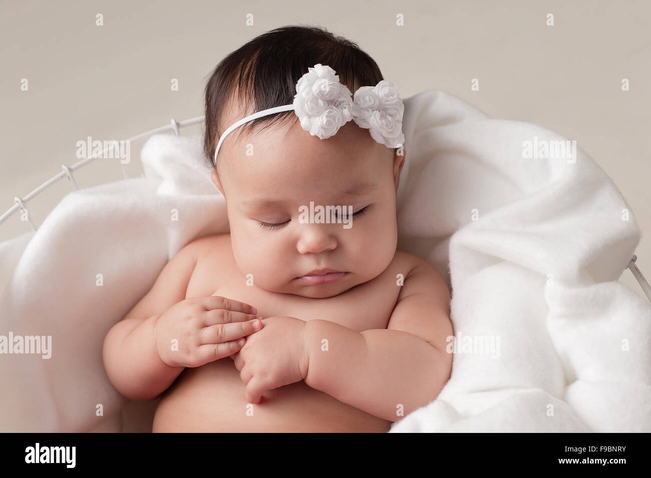 Vier Monate altes Baby Mädchen tragen eine weiße, Bogen Stirnband. Sie schläft auf weißem Stoff in einen Drahtkorb gesetzt. Gedreht in Stockfoto