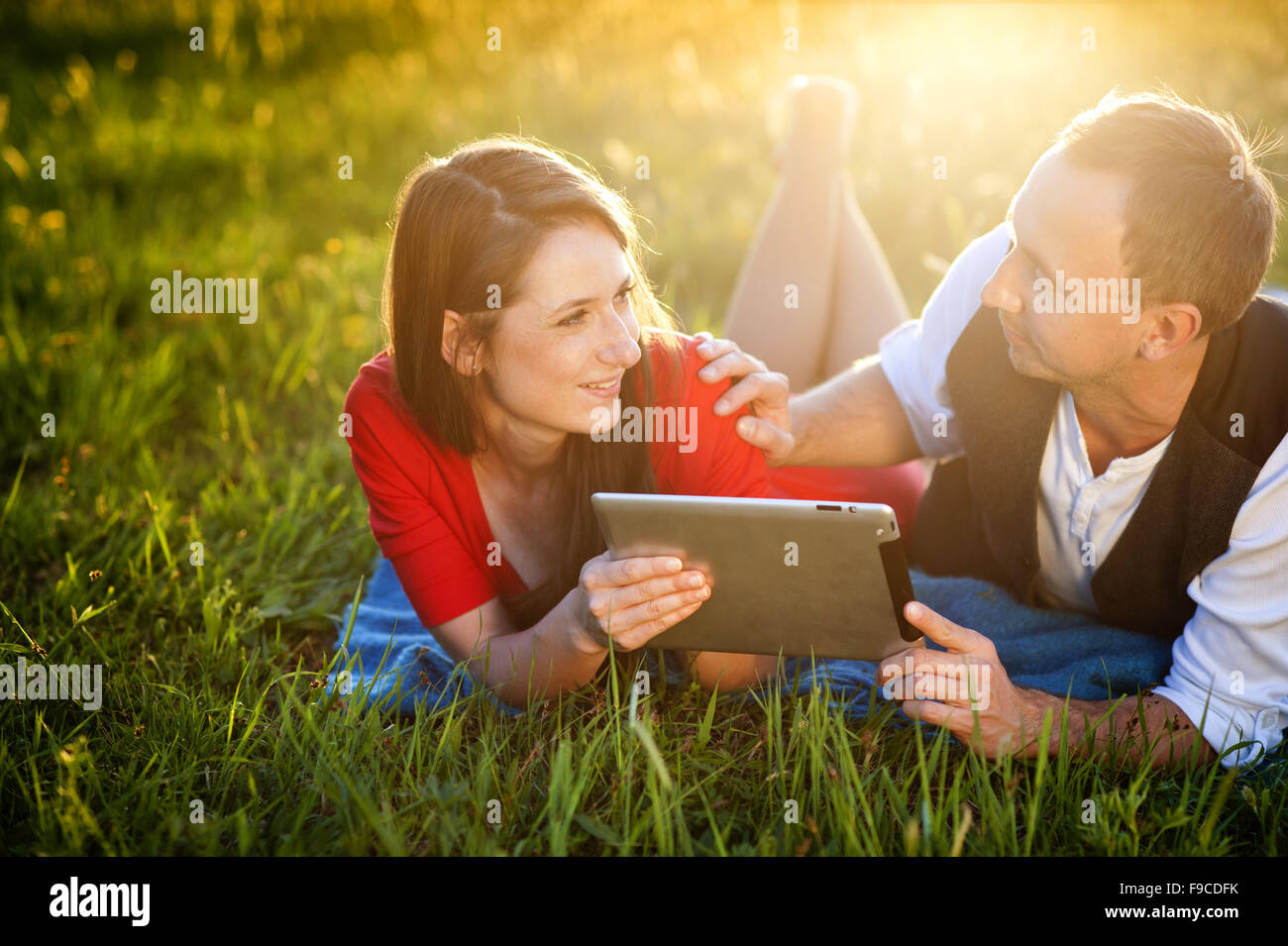 Glückliches Paar ist auf der Wiese liegen und spielen mit tablet Stockfoto