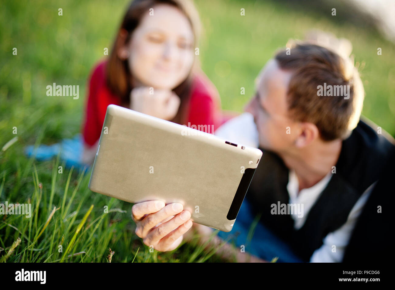 Glückliches Paar ist auf der Wiese liegen und spielen mit tablet Stockfoto