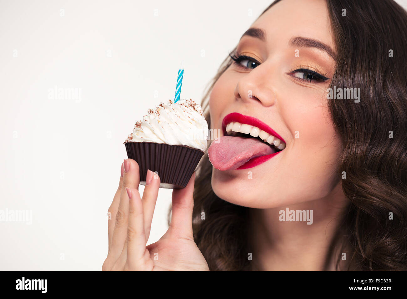 Nahaufnahme der schöne fröhliche junge Frau mit Retro-Frisur Essen Geburtstag Cupcake mit Kerze auf weißem Hintergrund Stockfoto