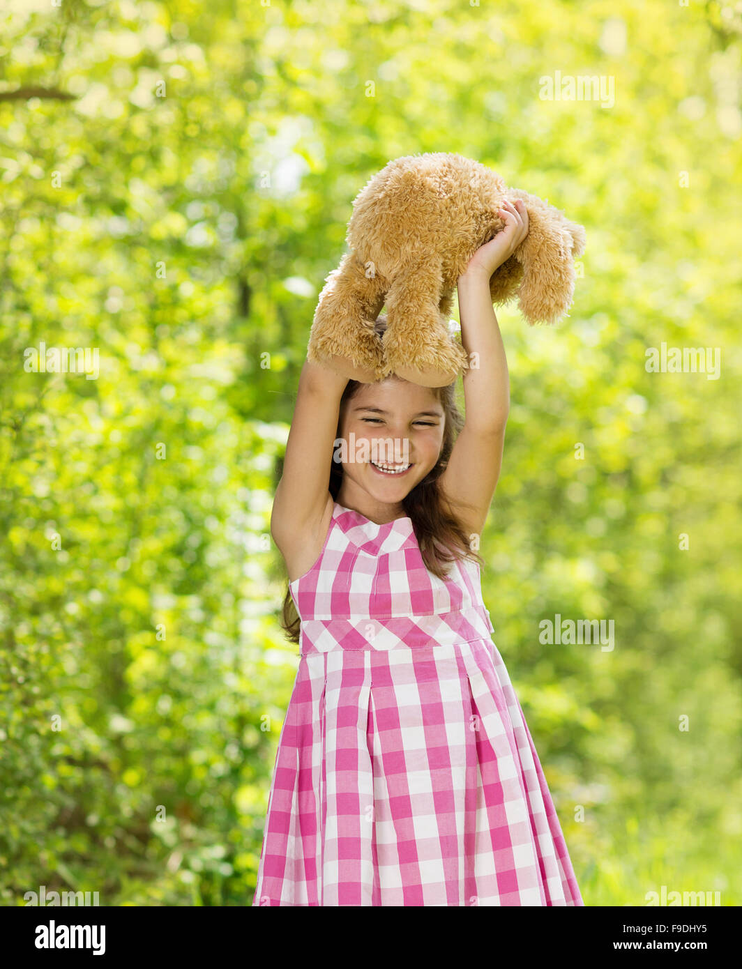 Niedliche kleine Mädchen im rosa Kleid spielt mit braunen Teddy in der grünen Natur Stockfoto