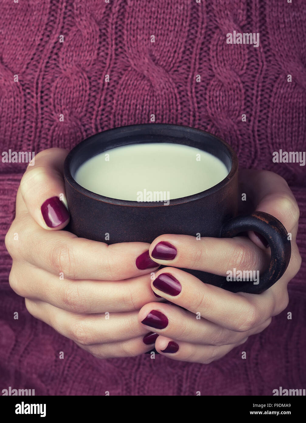 weibliche Hände in Burgund Pullover mit einer Ton-Tasse warme Milch Stockfoto