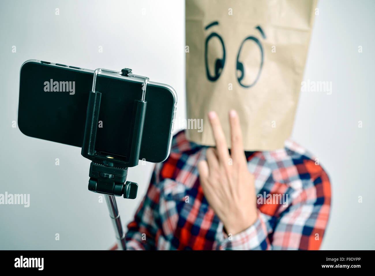 ein junger kaukasischer Mann mit einer Papiertüte mit lustigem Gesicht nimmt ein Selbstporträt mit einem Selfie Stock während gibt ein V-Zeichen Stockfoto