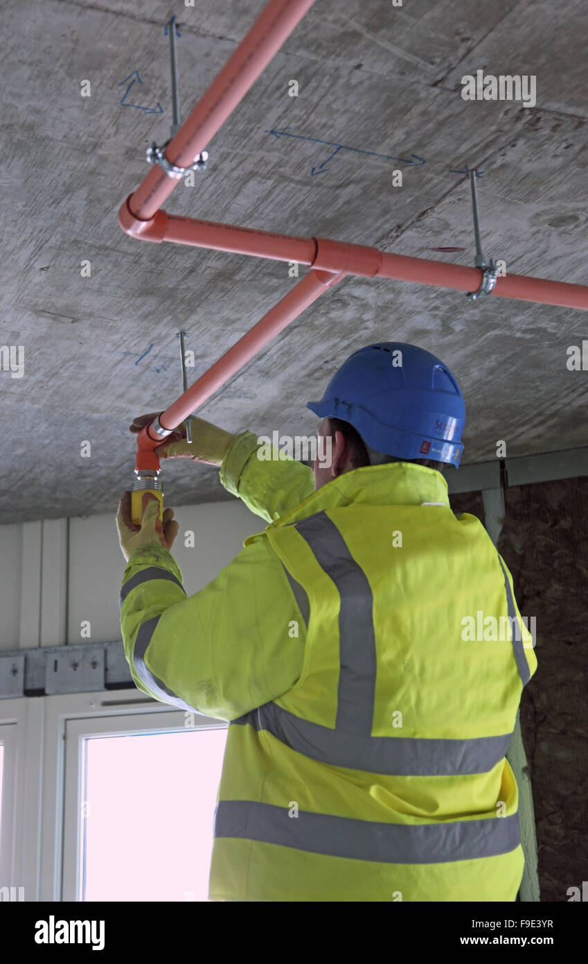 Ein Techniker installiert eine Sprinkleranlage unter einer Betonplatte in einem neuen Wohngebiet Tower in London, UK. Fertige Decke noch nicht montiert. Stockfoto