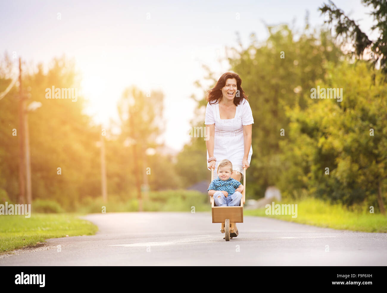 Glückliche junge Mutter mit ihrem Sohn draußen auf der Straße eines Dorfes spielen Stockfoto