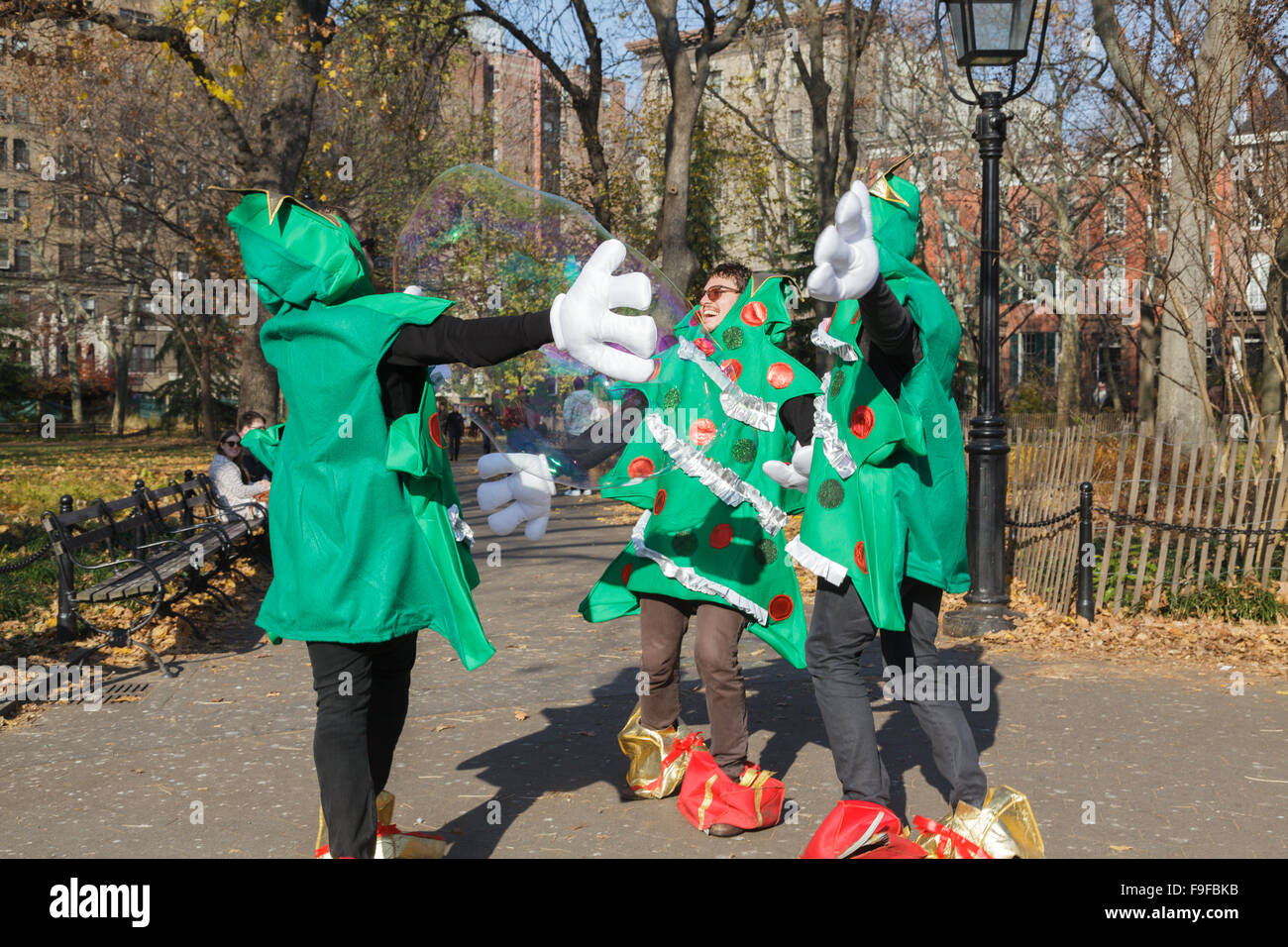 In Weihnachtskostüme gekleidete Männer jagen riesige Seifenblasen Washington Square, East Village, New York City, USA Stockfoto