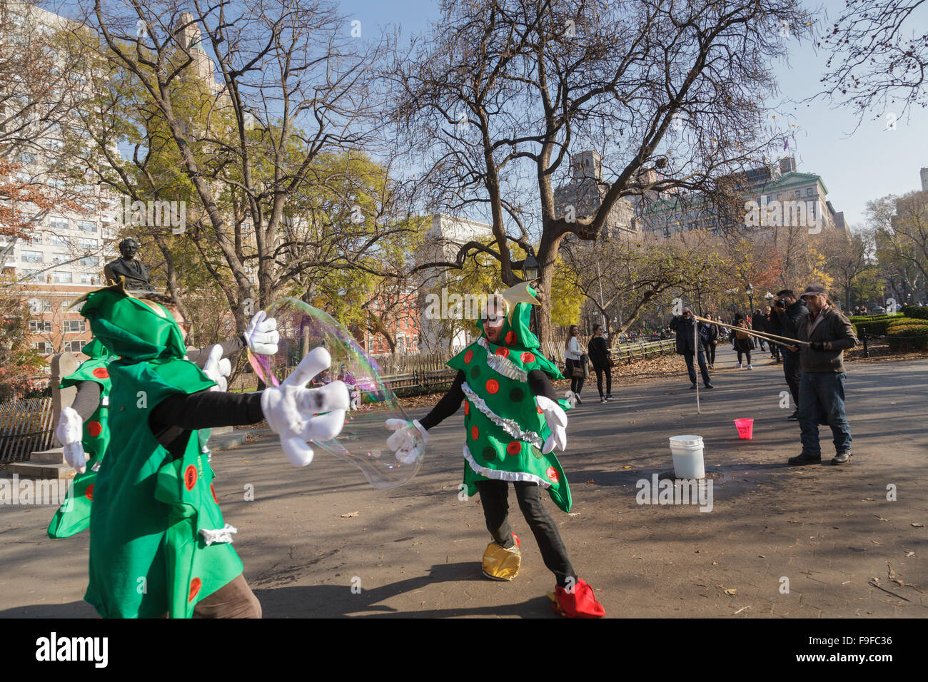 In Weihnachtskostüme gekleidete Männer jagen riesige Seifenblasen Washington Square, East Village, New York City, USA Stockfoto