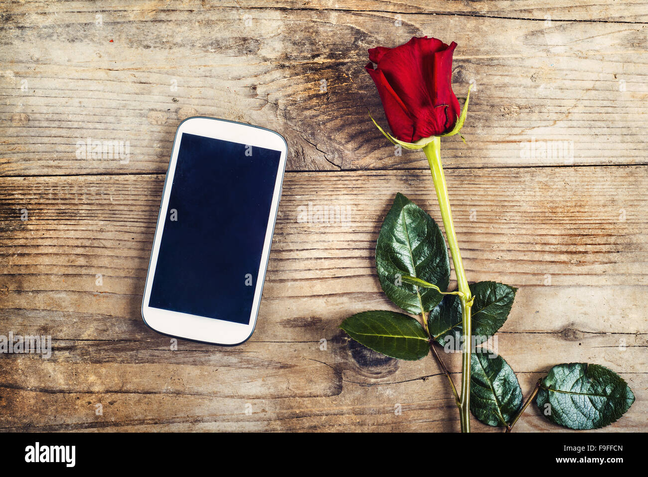 Valentins Tag Zusammensetzung noch nicht geschriebene Liebesbotschaft in ein Handy und eine rote Rose. Studio auf einem Holzboden Hintergrund gedreht. Stockfoto