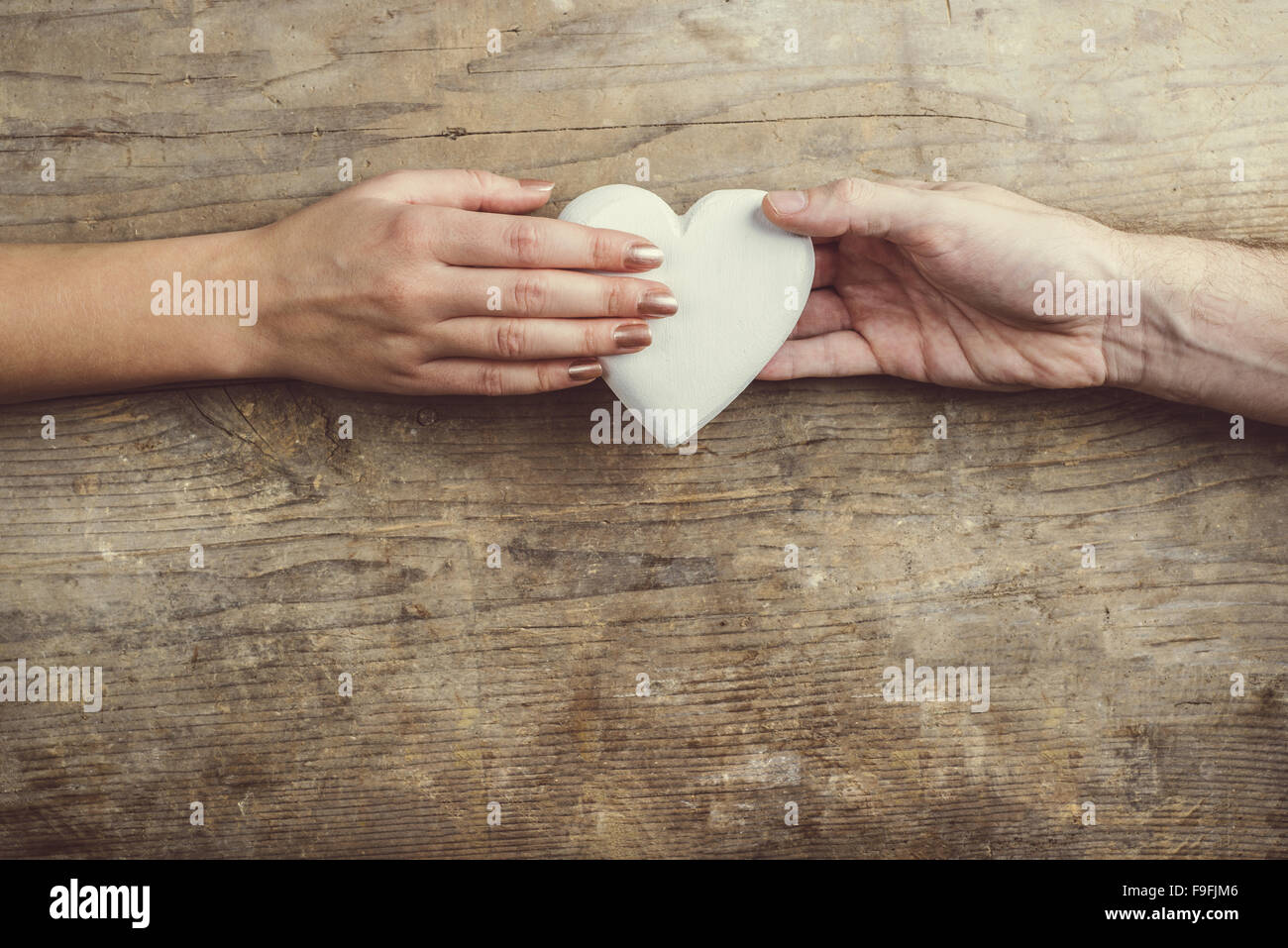 Hände von Mann und Frau durch ein weißes Herz verbunden. Studio auf einem hölzernen Hintergrund erschossen, Ansicht von oben. Stockfoto