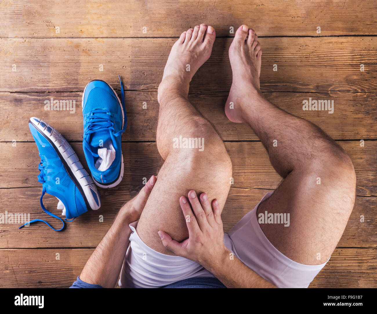 Nicht erkennbare verletzten Läufer sitzt auf einem Holzboden-Hintergrund Stockfoto
