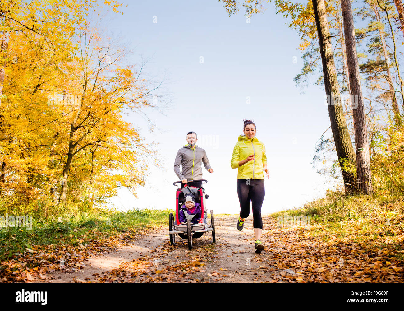 Schöne junge Familie mit Baby im Kinderwagen im Herbst Natur draußen laufen Joggen Stockfoto