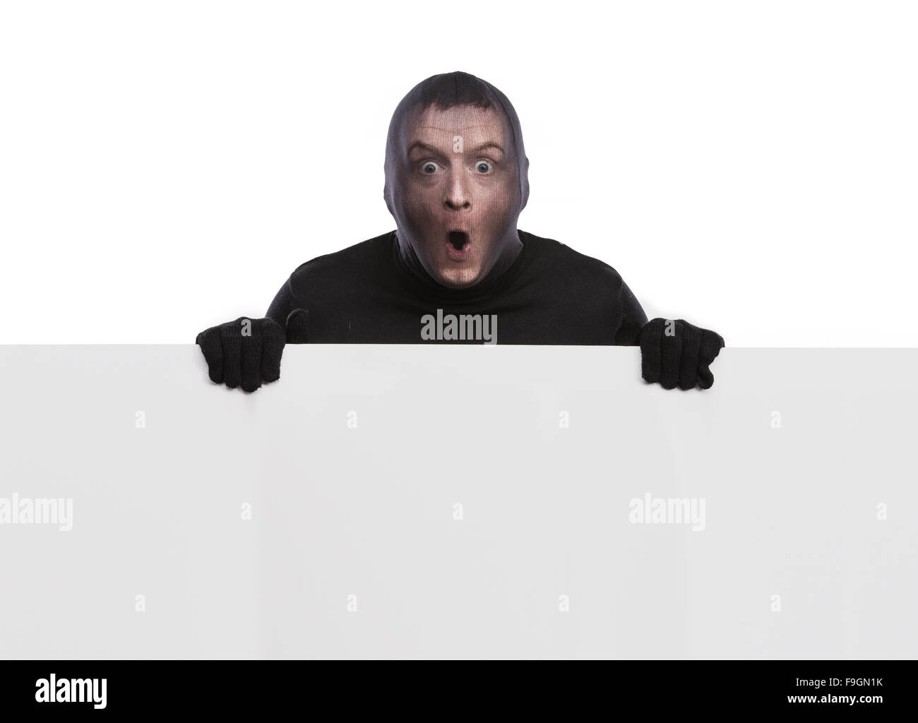 Dieb mit Sturmhaube auf seinem Gesicht, in schwarz gekleidet, hält einen leere Banner. Studio auf weißem Hintergrund gedreht. Stockfoto