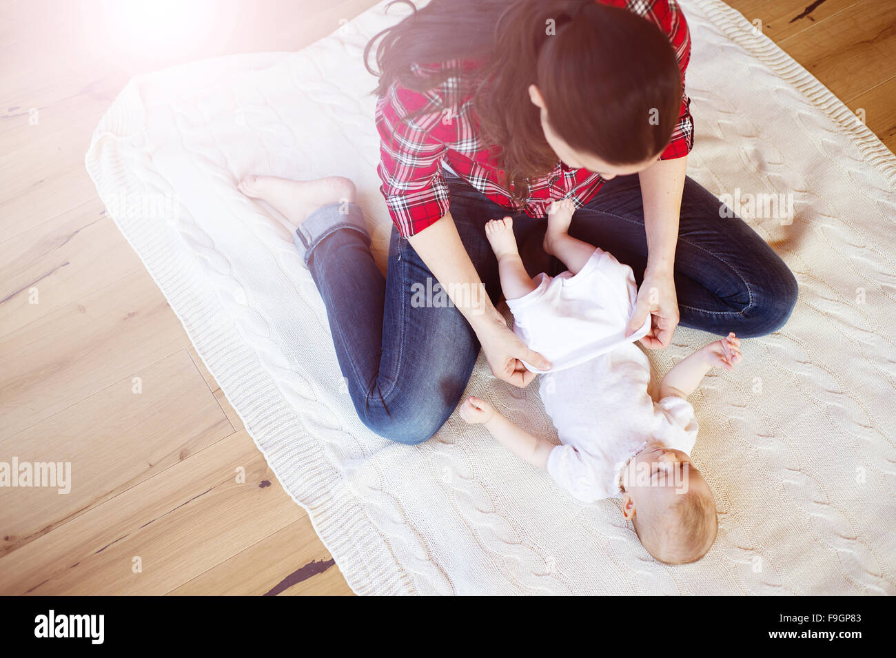 Niedliche kleine Baby Mädchen ankleiden von der Mutter auf einem Teppich im Wohnzimmer. Stockfoto