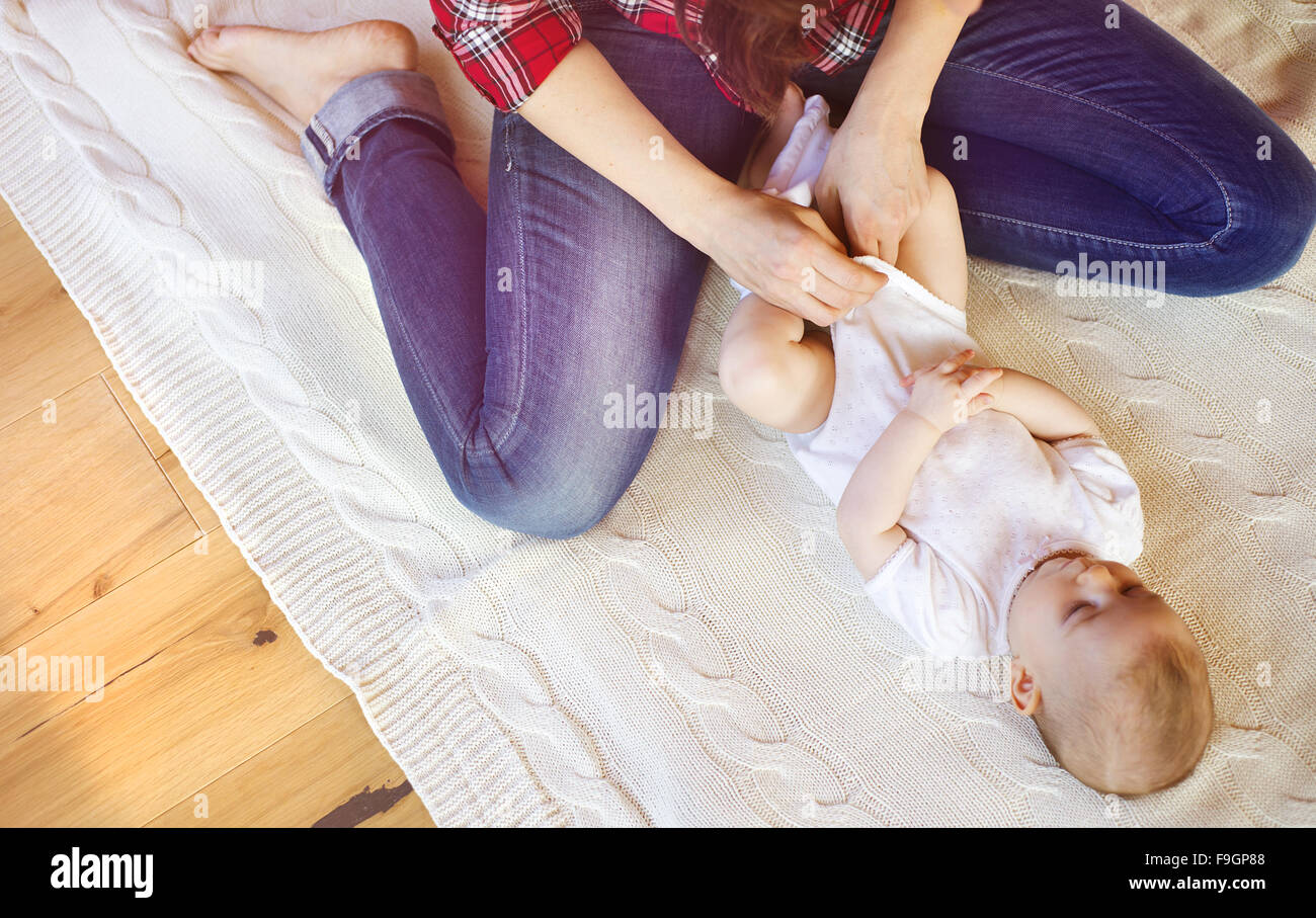 Niedliche kleine Baby Mädchen ankleiden von der Mutter auf einem Teppich im Wohnzimmer. Stockfoto