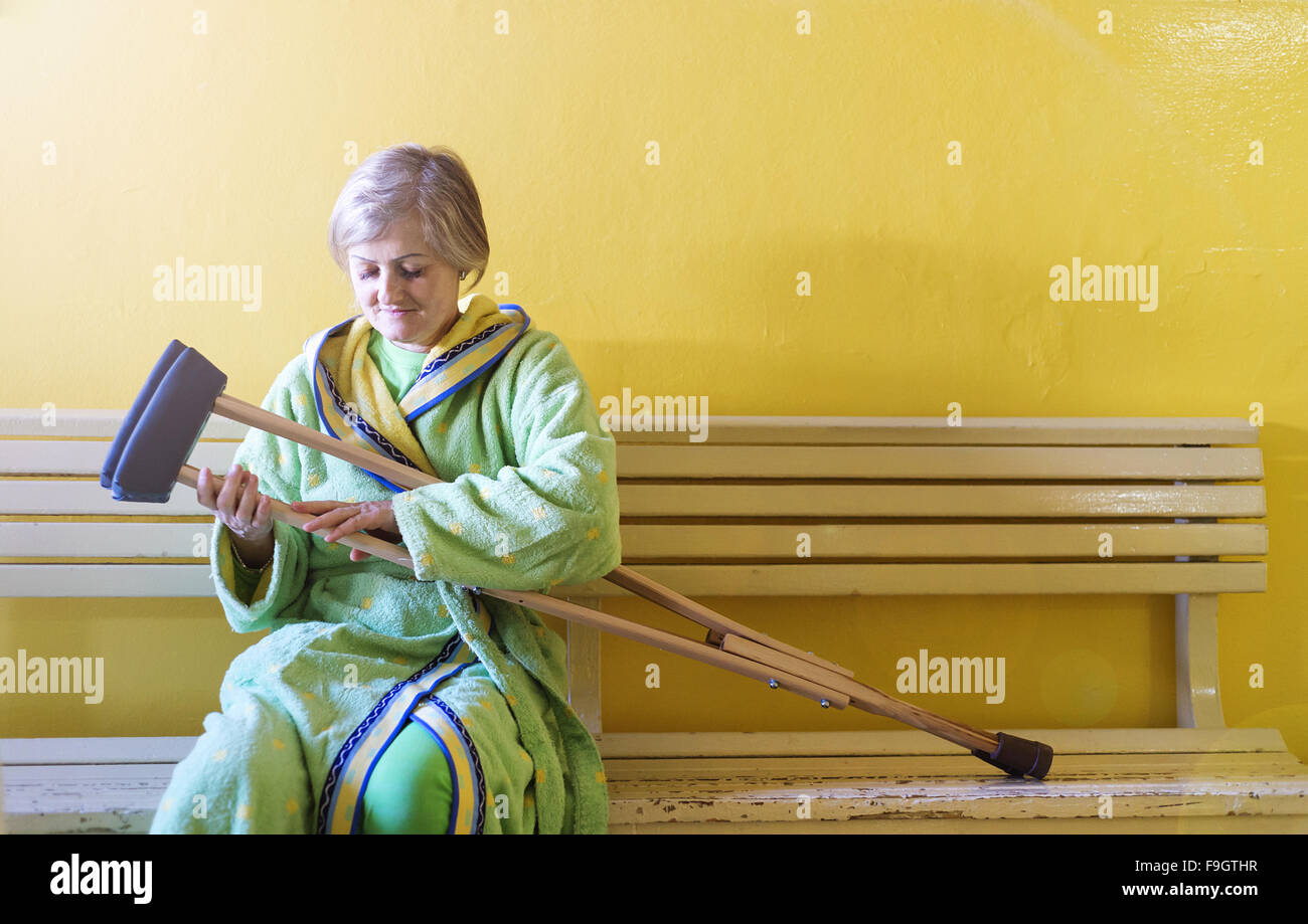 Ältere Frau verletzt sitzen auf dem Flur des Krankenhauses mit Krücken Stockfoto