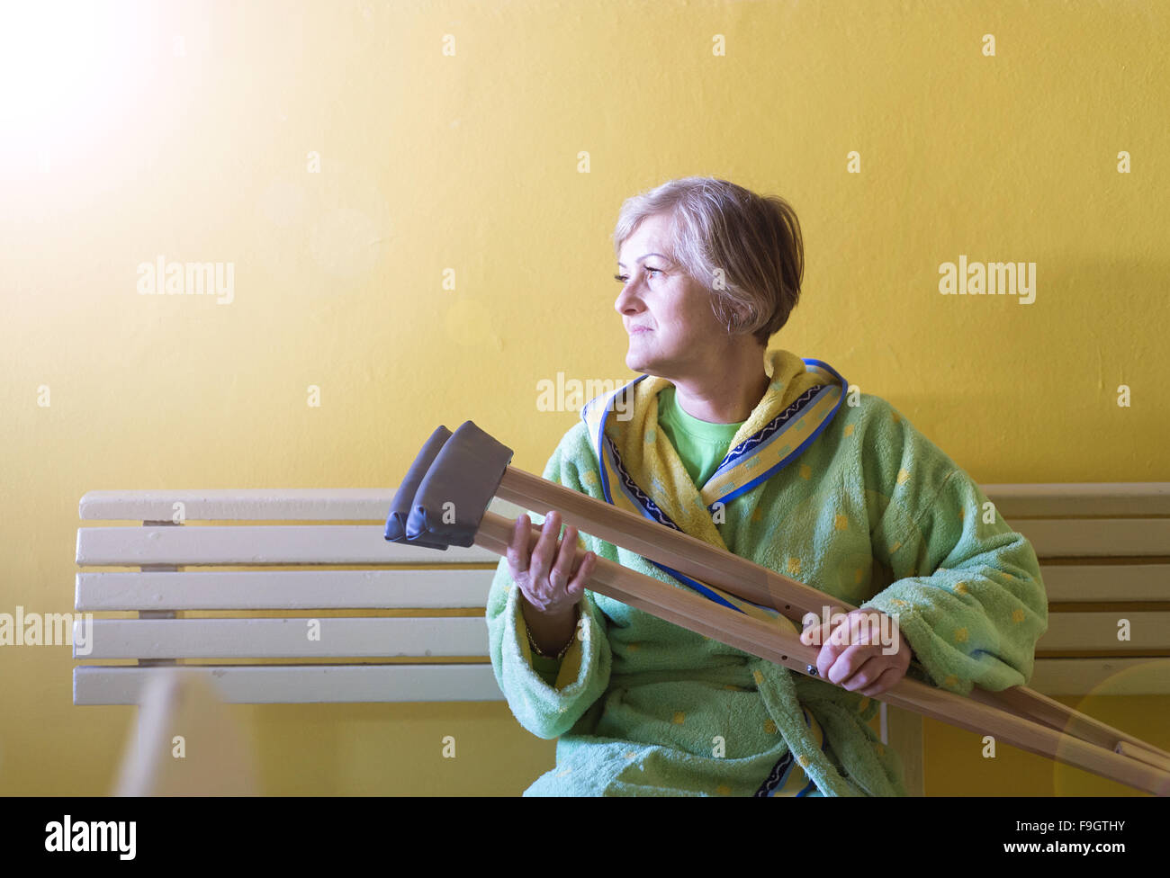 Ältere Frau verletzt sitzen auf dem Flur des Krankenhauses mit Krücken Stockfoto