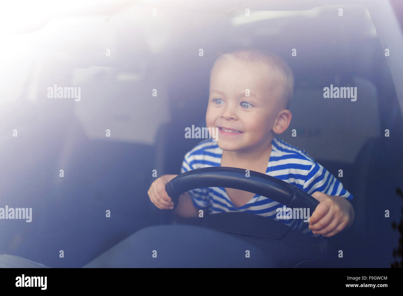 Kleiner Junge spielt mit einem Lenkrad im Auto Stockfoto