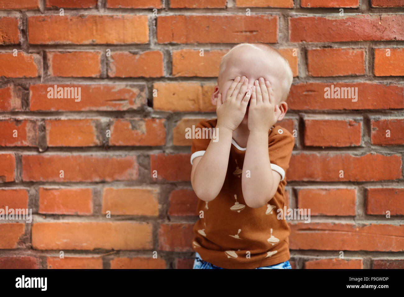 Niedliche kleine junge lustige Grimassen auf einer gemauerten Wand Hintergrund Stockfoto