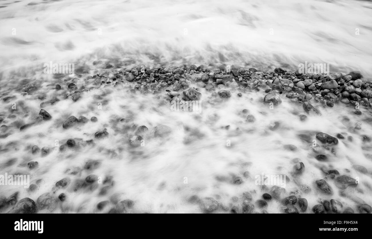 Geheimnisvolle schwarze und weiße Langzeitbelichtung Schuss aus Kieselsteinen am ruhigen Strand in der Nähe von Meer Stockfoto