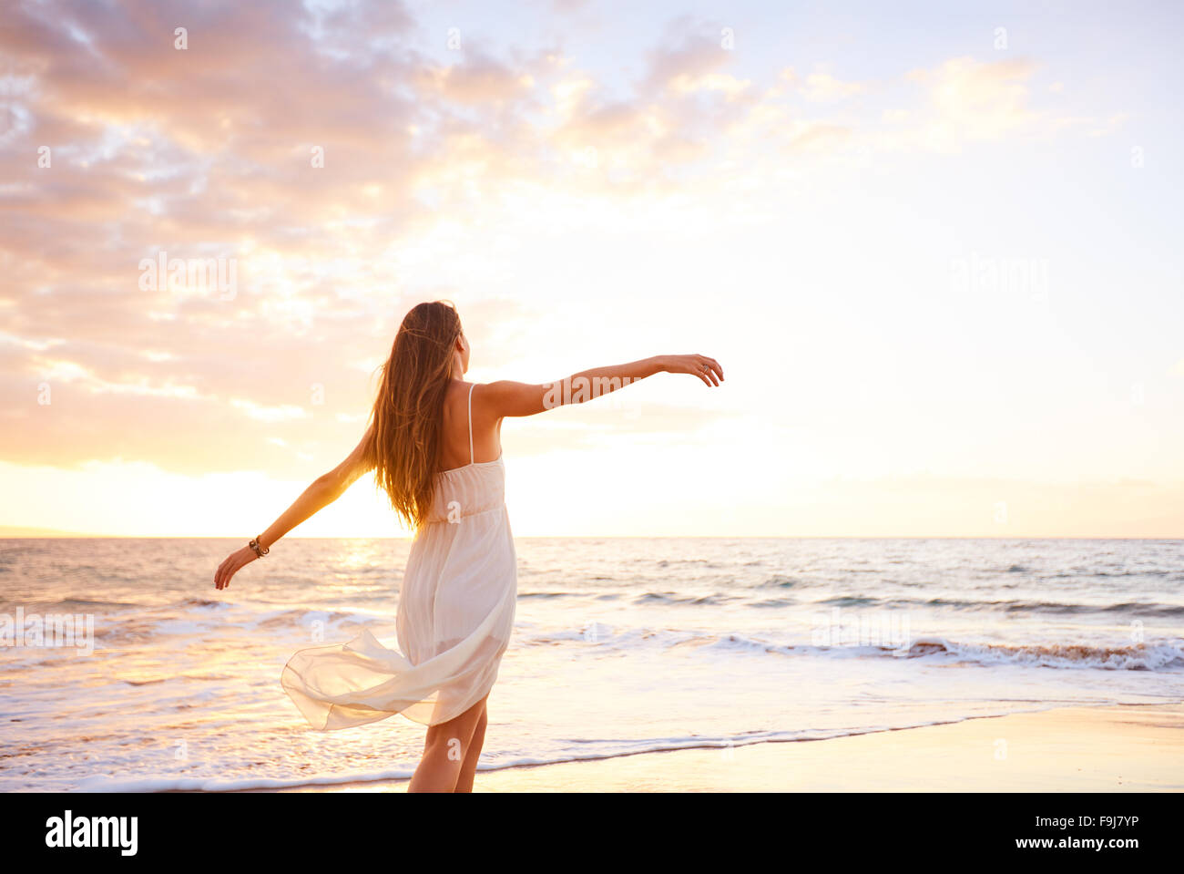 Fröhliche unbeschwerte Frau tanzen bei Sonnenuntergang am Strand. Glücklich kostenlose Lifestyle-Konzept. Stockfoto