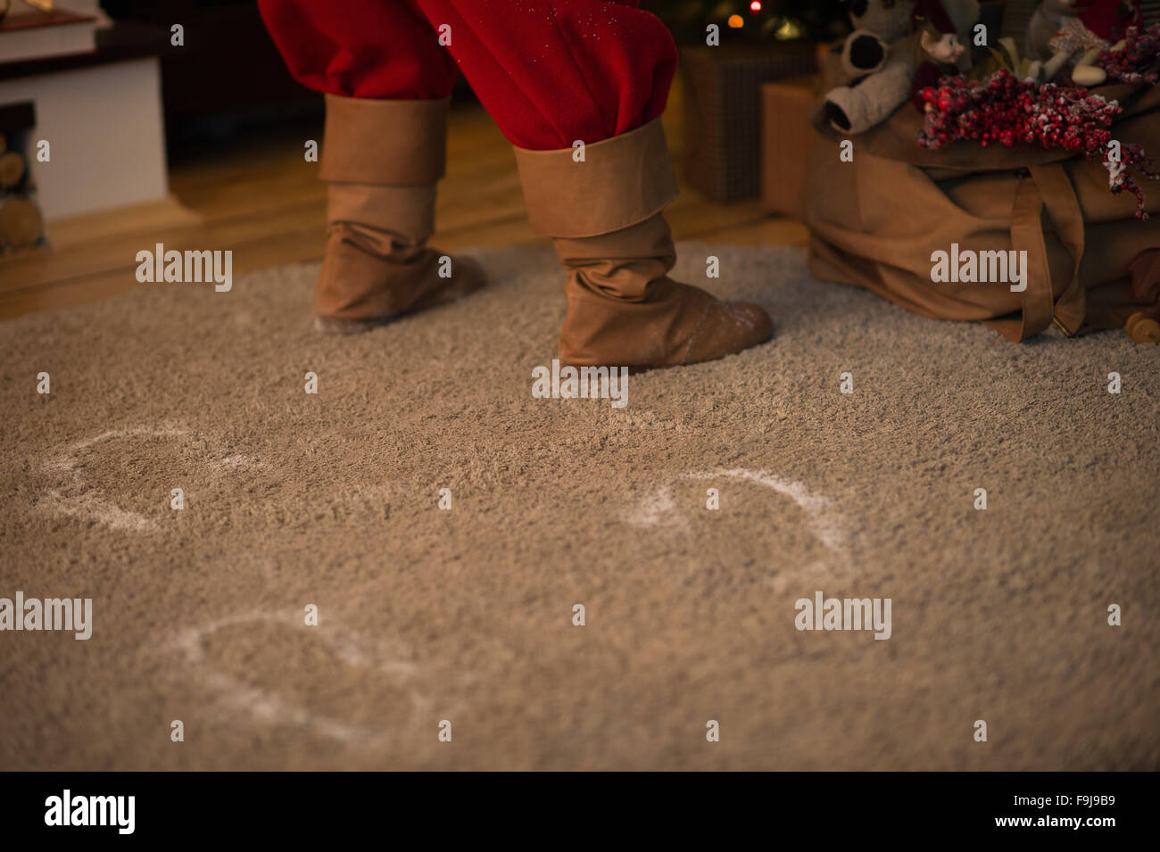 Santa Claus zu Hause setzen Geschenke unter dem Weihnachtsbaum. Schnee-Spuren auf Teppich Stockfoto