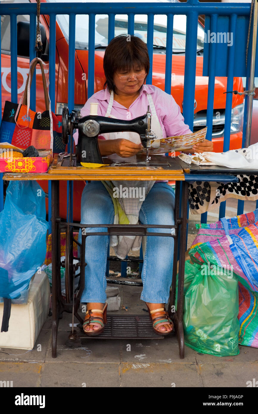Ein weiblicher Schneider betreibt eine kleine Outdoor-Nähmaschine auf Bürgersteig der Innenstadt Straße in der informellen Wirtschaft Stockfoto
