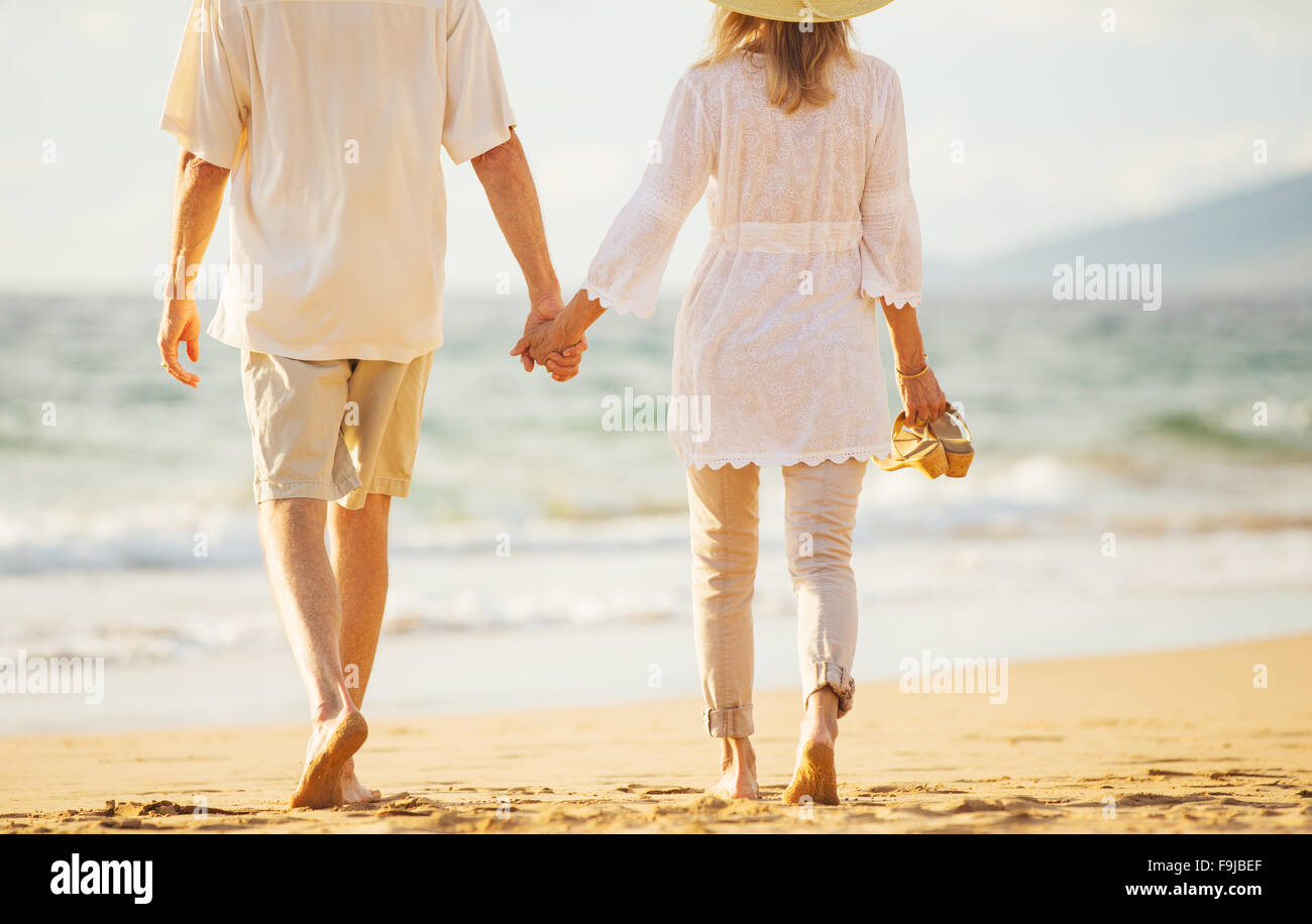 Glückliche romantische mittleren gealterten paar schönen Sonnenuntergang genießen Strandspaziergang Hand in Hand Stockfoto
