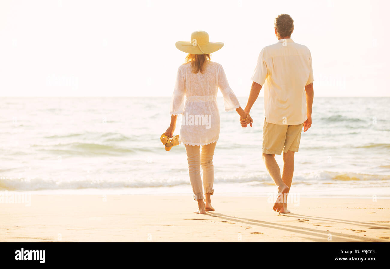 Glückliche romantische mittleren gealterten paar schönen Sonnenuntergang genießen Strandspaziergang Hand in Hand Stockfoto