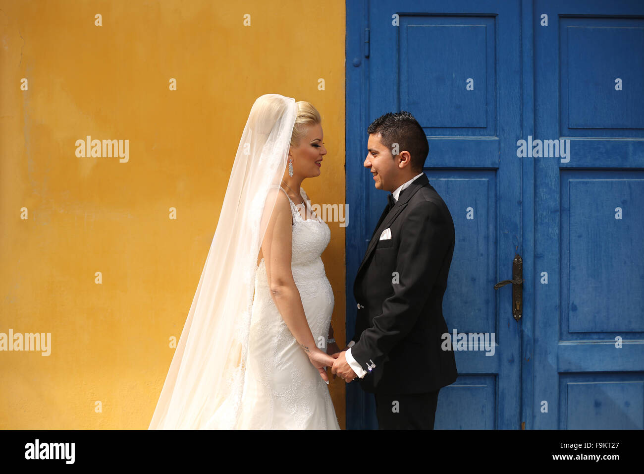 Schöne Braut und Bräutigam Hand in Hand neben bunten Tür und Wand Stockfoto