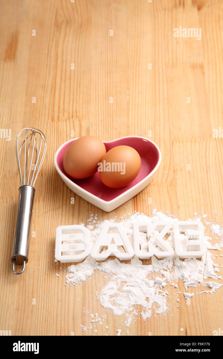Backen, Konzept, Hand Schneebesen und Eiern in einem Herz-Form-container Stockfoto