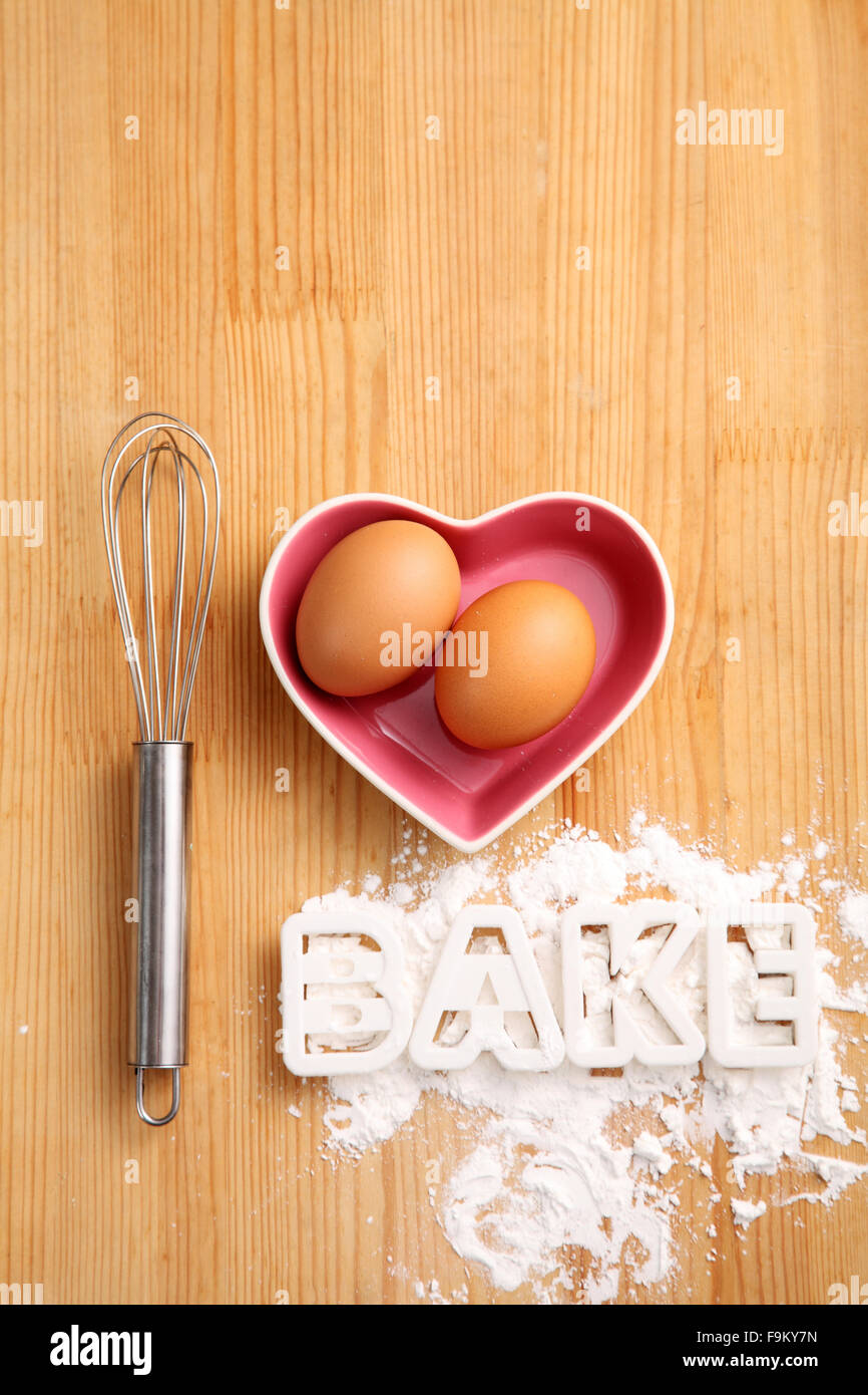 Backen, Konzept, Hand Schneebesen und Eiern in einem Herz-Form-container Stockfoto