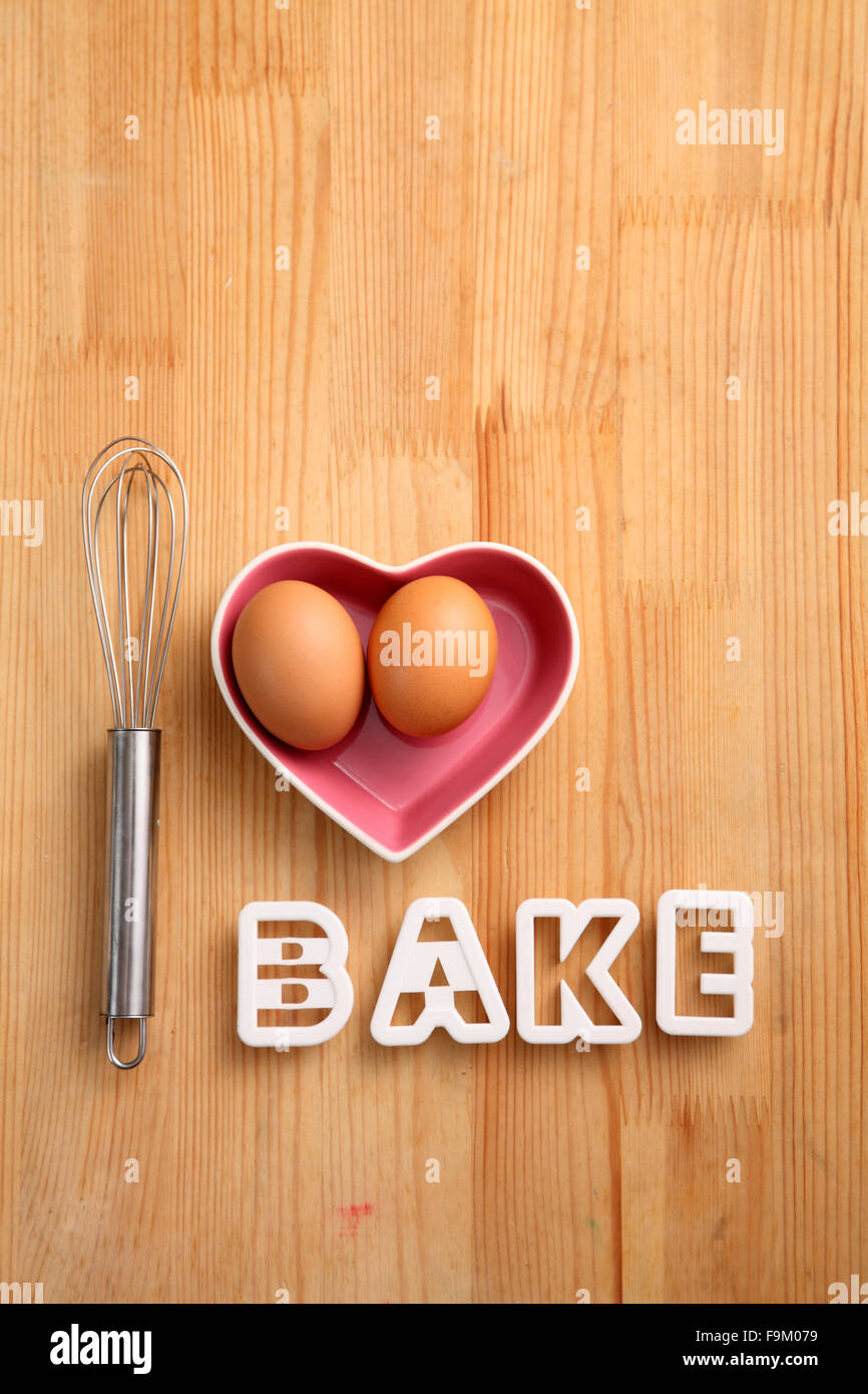 Backen Konzept Hand Schneebesen neben Eiern in einem Herz-Form-container Stockfoto