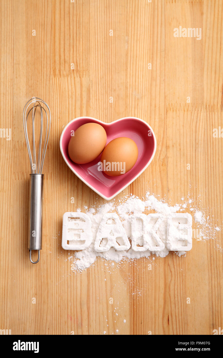 Backen, Konzept, Hand Schneebesen und Eiern in einem Herz-Form-container Stockfoto