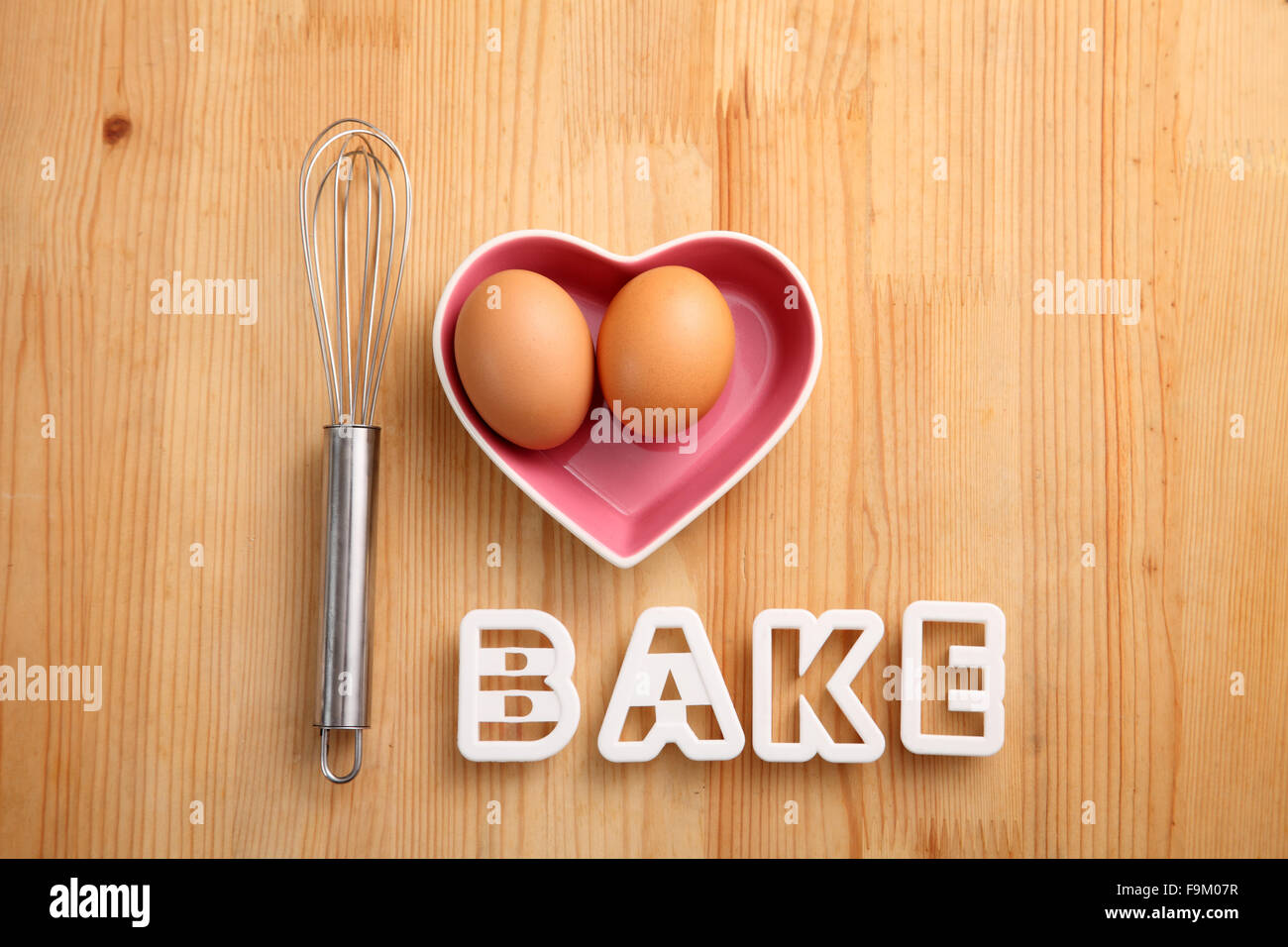 Backen Konzept Hand Schneebesen neben Eiern in einem Herz-Form-container Stockfoto