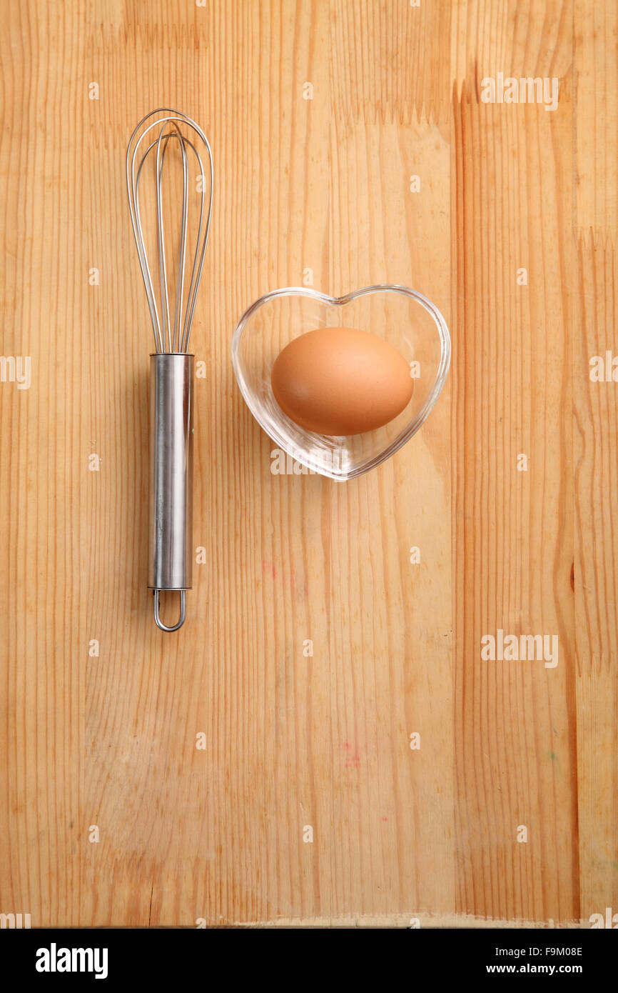 Backen Konzept Hand Schneebesen neben Ei in einem Herz-Form-container Stockfoto