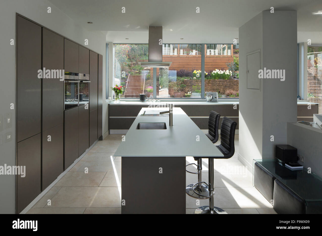 Einen großen offenen Raum, Küche und Essbereich, mit Ansichten aus dem vollen Größe Glas Wandpaneele auf einen Patio. Minimalistische, klare Linien und schlichte Wände. Stockfoto