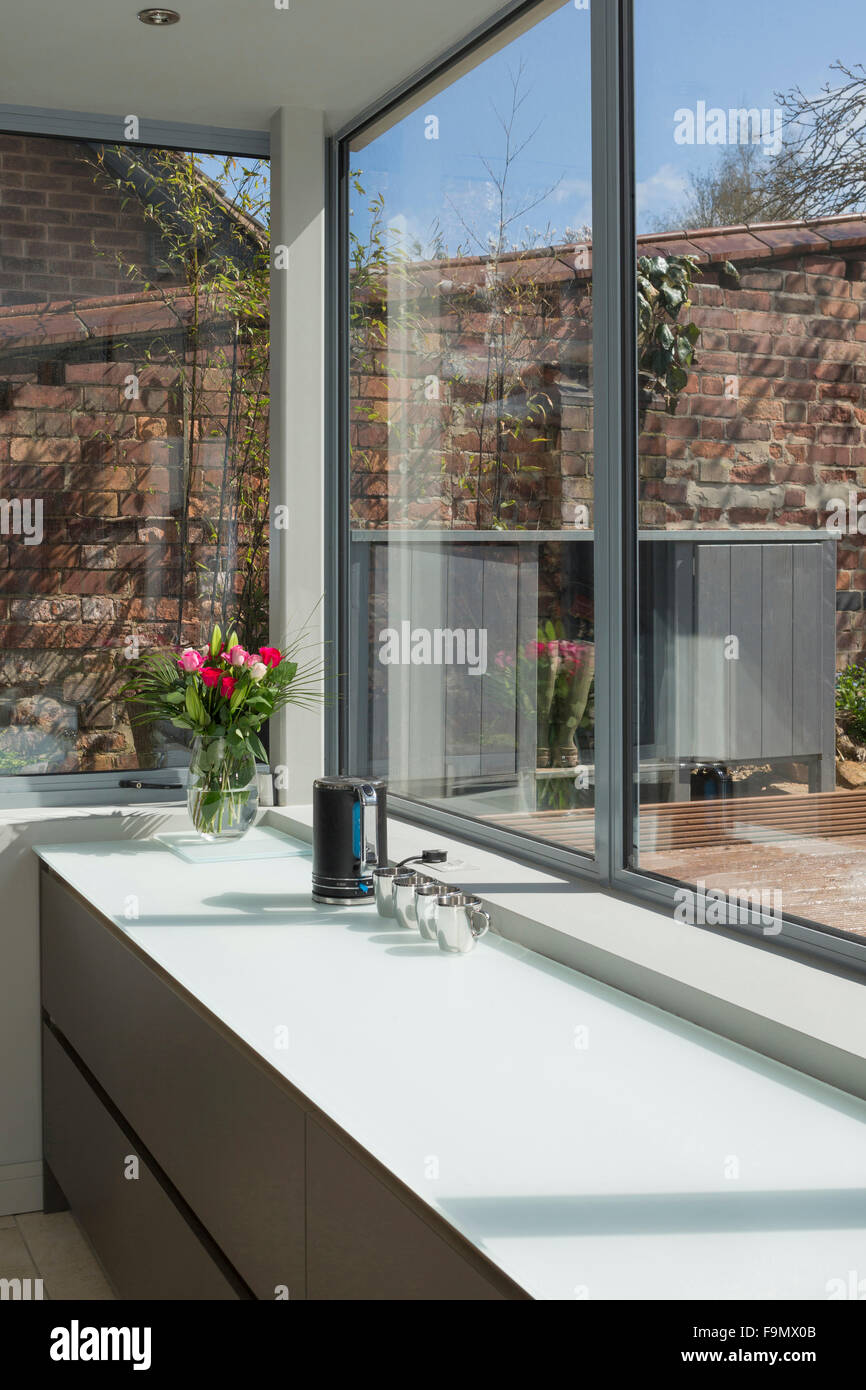 Einen großen offenen Raum, Küche und Essbereich, mit Ansichten aus dem vollen Größe Glas Wandpaneele auf einen Patio. Minimalistische, klare Linien und schlichte Wände. Stockfoto