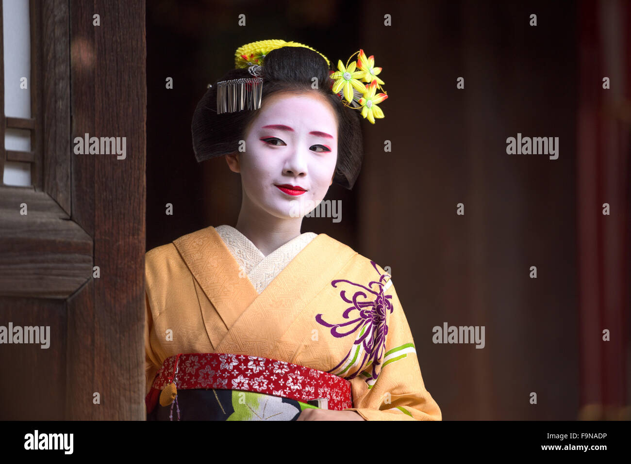 Eine Frau gekleidet wie eine traditionelle Maiko aus einem Eingang Tempel in Kyoto, Japan aussieht. Stockfoto