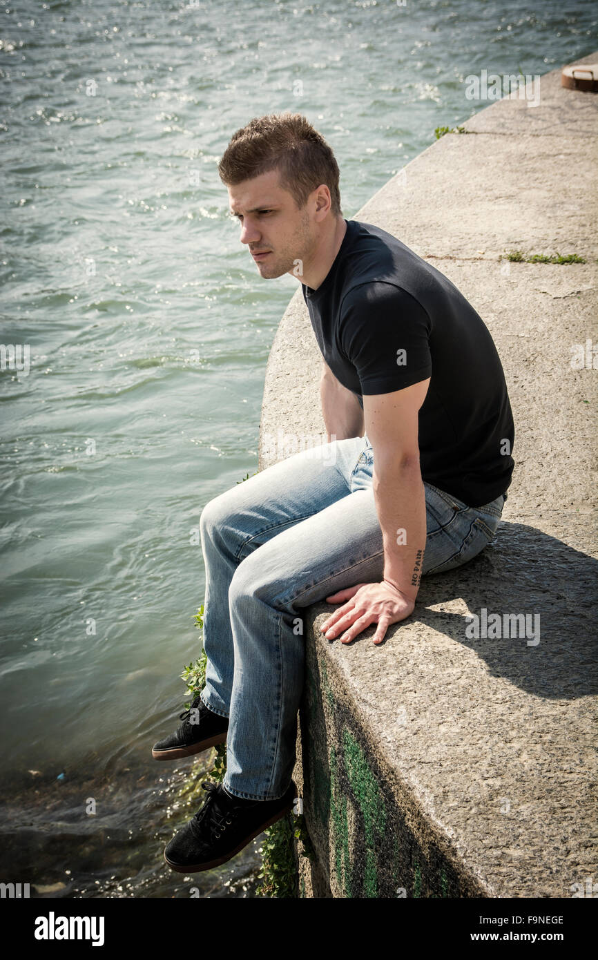 3/4 Länge des kontemplativen Licht braun behaarte Teenager tragen grüne Kapuzen-Shirt und Jeans Jeans sitzen auf Wand Stockfoto