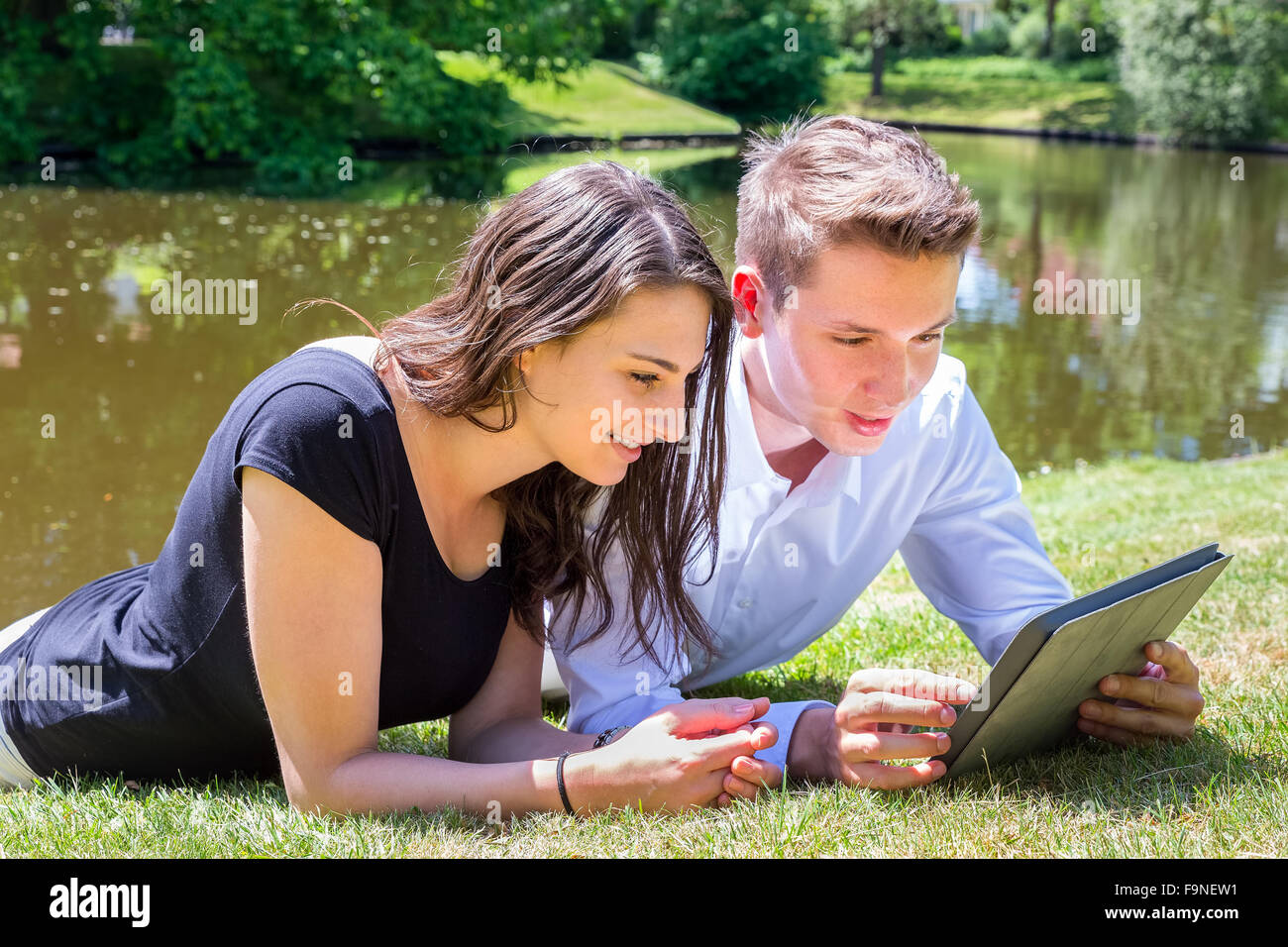 Junges Paar liegen auf dem Rasen am Wasser Ipad lesen Stockfoto