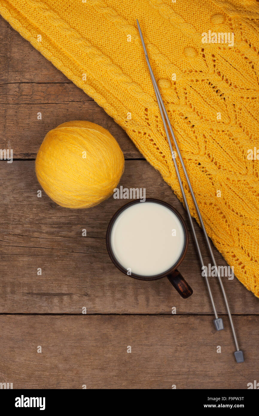 gelbe Strickpullover und einem Knäuel für stricken und eine Tasse warme Milch auf dem Holztisch Stockfoto